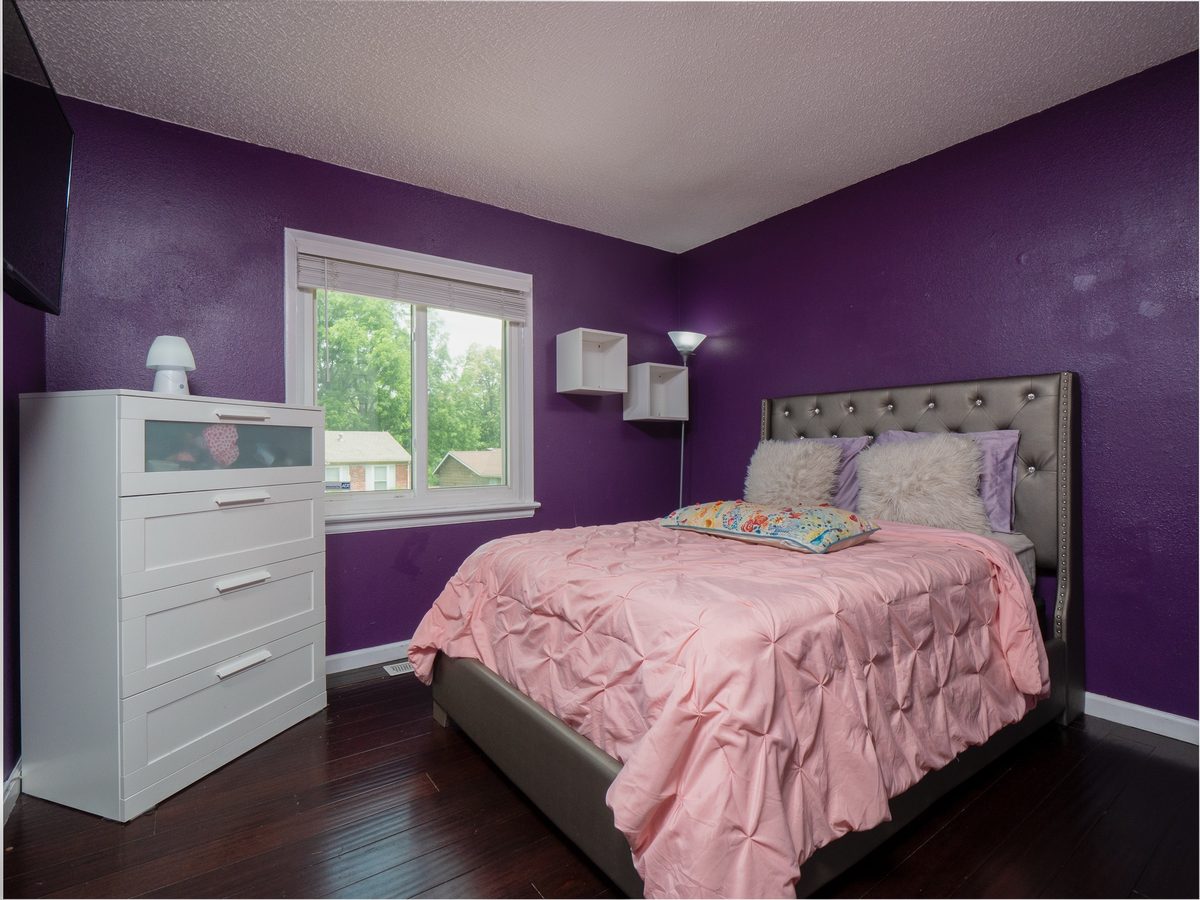 A bedroom at 12945 Covington Gardens Drive with purple walls, dark wood floors, a white dresser and a tufted headboard