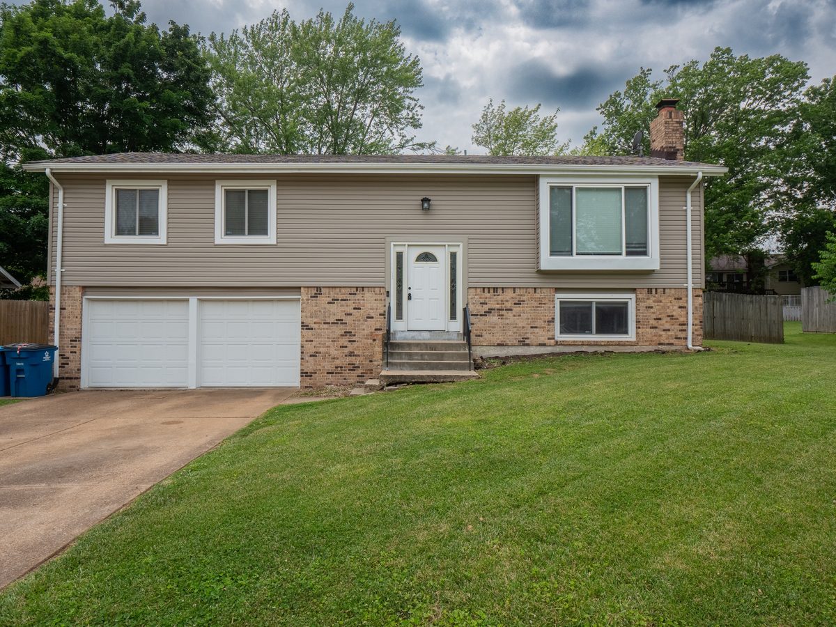 12945 Covington Gardens Drive: a split-foyer home with tan vinyl siding, a brick lower level, a two-car garage and a wide front lawn