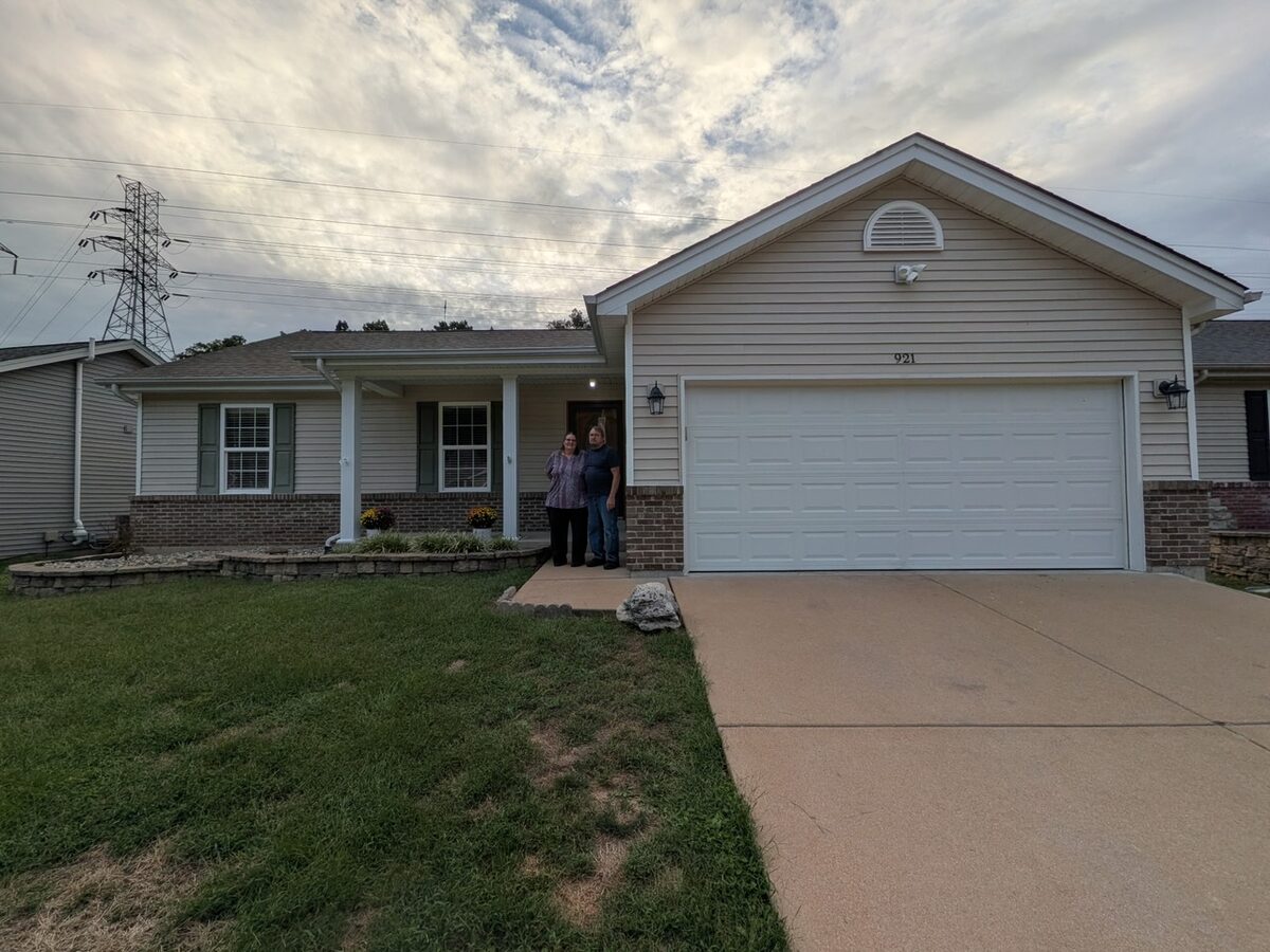 Roy and Karen standing on the front porch of their ranch home at 921 San Luis Drive in Fenton, Missouri, with a two-car garage and the spotlight above it