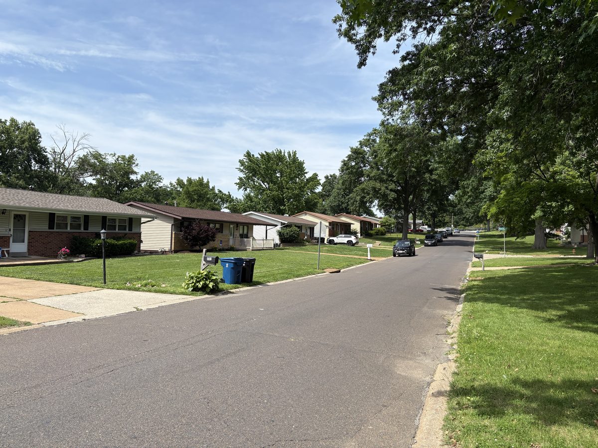 Oakville St. Louis neighborhood — brick and vinyl ranch homes on large lots with mature oak canopy, 63129 South County residential street
